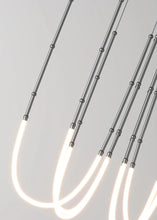 Load image into Gallery viewer, Siliq Sculptural Light with handcrafted silicone forms and metallic segmented cables, single minimalist pendant with glowing silicone tube, dramatic chandelier version of Siliq Light for high ceilings, floor-to-ceiling sculptural lighting installation in modern interior, flexible silicone light tubes emitting soft ambient glow, artistic designer light fixture styled in dining room, contemporary sculptural lighting as statement piece in commercial space.