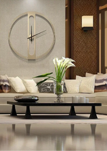 Load image into Gallery viewer, INSPIRA LIFESTYLES - Xavier Wall Clock, extra large wall clock, modern iron wall clock, sculptural wall decor, gold wall clock, charcoal wall clock, minimalist timepiece, statement wall accent, living room clock, office wall clock, oversized modern clock. Modern living room with a clock on the wall, a sofa, and a coffee table.
