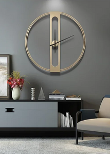 INSPIRA LIFESTYLES - Xavier Wall Clock, extra large wall clock, modern iron wall clock, sculptural wall decor, gold wall clock, charcoal wall clock, minimalist timepiece, statement wall accent, living room clock, office wall clock, oversized modern clock Modern wall clock on a gray wall with a decorative setup including books, a vase, and a chair.