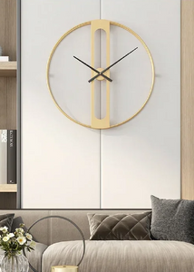 INSPIRA LIFESTYLES - Xavier Wall Clock, extra large wall clock, modern iron wall clock, sculptural wall decor, gold wall clock, charcoal wall clock, minimalist timepiece, statement wall accent, living room clock, office wall clock, oversized modern clock Gold wall clock on a white wall above a gray sofa with decorative elements.