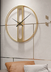 INSPIRA LIFESTYLES - Xavier Wall Clock, extra large wall clock, modern iron wall clock, sculptural wall decor, gold wall clock, charcoal wall clock, minimalist timepiece, statement wall accent, living room clock, office wall clock, oversized modern clock Gold wall clock on a textured wall with pillows at the bottom.