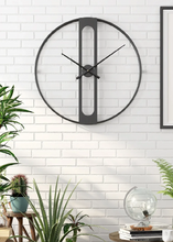 Load image into Gallery viewer, INSPIRA LIFESTYLES - Xavier Wall Clock, extra large wall clock, modern iron wall clock, sculptural wall decor, gold wall clock, charcoal wall clock, minimalist timepiece, statement wall accent, living room clock, office wall clock, oversized modern clock Large round wall clock on a white brick wall with plants and decor below.
