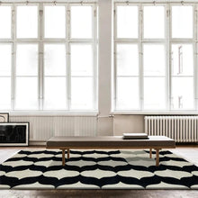 Load image into Gallery viewer, INSPIRA LIFESTYLES – Monarc Area Rug, black and ivory geometric rug, 100% polyester rug, soft and durable area rug, modern patterned rug, abstract design rug, contemporary interior rug, high-performance rug, easy-clean rug, living room rug, dining room rug, designer rug décor. Modern living room with a black and white patterned rug, wooden bench, and large windows.
