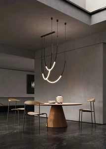 Siliq Sculptural Light with handcrafted silicone forms and metallic segmented cables, single minimalist pendant with glowing silicone tube, dramatic chandelier version of Siliq Light for high ceilings, floor-to-ceiling sculptural lighting installation in modern interior, flexible silicone light tubes emitting soft ambient glow, artistic designer light fixture styled in dining room, contemporary sculptural lighting as statement piece in commercial space.