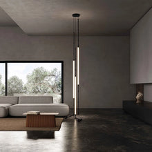 Load image into Gallery viewer, Siliq Sculptural Light with handcrafted silicone forms and metallic segmented cables, single minimalist pendant with glowing silicone tube, dramatic chandelier version of Siliq Light for high ceilings, floor-to-ceiling sculptural lighting installation in modern interior, flexible silicone light tubes emitting soft ambient glow, artistic designer light fixture styled in dining room, contemporary sculptural lighting as statement piece in commercial space. Modern living room with a floor lamp and large window
