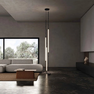 Siliq Sculptural Light with handcrafted silicone forms and metallic segmented cables, single minimalist pendant with glowing silicone tube, dramatic chandelier version of Siliq Light for high ceilings, floor-to-ceiling sculptural lighting installation in modern interior, flexible silicone light tubes emitting soft ambient glow, artistic designer light fixture styled in dining room, contemporary sculptural lighting as statement piece in commercial space. Modern living room with a floor lamp and large window