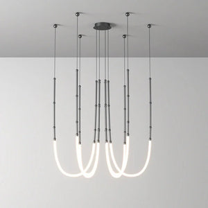 Siliq Sculptural Light with handcrafted silicone forms and metallic segmented cables, single minimalist pendant with glowing silicone tube, dramatic chandelier version of Siliq Light for high ceilings, floor-to-ceiling sculptural lighting installation in modern interior, flexible silicone light tubes emitting soft ambient glow, artistic designer light fixture styled in dining room, contemporary sculptural lighting as statement piece in commercial space.