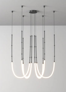 Siliq Sculptural Light with handcrafted silicone forms and metallic segmented cables, single minimalist pendant with glowing silicone tube, dramatic chandelier version of Siliq Light for high ceilings, floor-to-ceiling sculptural lighting installation in modern interior, flexible silicone light tubes emitting soft ambient glow, artistic designer light fixture styled in dining room, contemporary sculptural lighting as statement piece in commercial space.