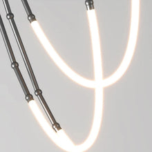 Load image into Gallery viewer, Siliq Sculptural Light with handcrafted silicone forms and metallic segmented cables, single minimalist pendant with glowing silicone tube, dramatic chandelier version of Siliq Light for high ceilings, floor-to-ceiling sculptural lighting installation in modern interior, flexible silicone light tubes emitting soft ambient glow, artistic designer light fixture styled in dining room, contemporary sculptural lighting as statement piece in commercial space.
