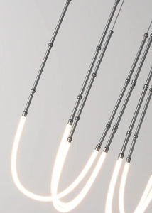 Siliq Sculptural Light with handcrafted silicone forms and metallic segmented cables, single minimalist pendant with glowing silicone tube, dramatic chandelier version of Siliq Light for high ceilings, floor-to-ceiling sculptural lighting installation in modern interior, flexible silicone light tubes emitting soft ambient glow, artistic designer light fixture styled in dining room, contemporary sculptural lighting as statement piece in commercial space.