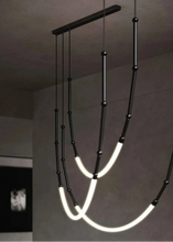 Load image into Gallery viewer, Siliq Sculptural Light with handcrafted silicone forms and metallic segmented cables, single minimalist pendant with glowing silicone tube, dramatic chandelier version of Siliq Light for high ceilings, floor-to-ceiling sculptural lighting installation in modern interior, flexible silicone light tubes emitting soft ambient glow, artistic designer light fixture styled in dining room, contemporary sculptural lighting as statement piece in commercial space.
