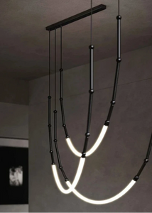 Siliq Sculptural Light with handcrafted silicone forms and metallic segmented cables, single minimalist pendant with glowing silicone tube, dramatic chandelier version of Siliq Light for high ceilings, floor-to-ceiling sculptural lighting installation in modern interior, flexible silicone light tubes emitting soft ambient glow, artistic designer light fixture styled in dining room, contemporary sculptural lighting as statement piece in commercial space.
