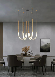Siliq Sculptural Light with handcrafted silicone forms and metallic segmented cables, single minimalist pendant with glowing silicone tube, dramatic chandelier version of Siliq Light for high ceilings, floor-to-ceiling sculptural lighting installation in modern interior, flexible silicone light tubes emitting soft ambient glow, artistic designer light fixture styled in dining room, contemporary sculptural lighting as statement piece in commercial space.