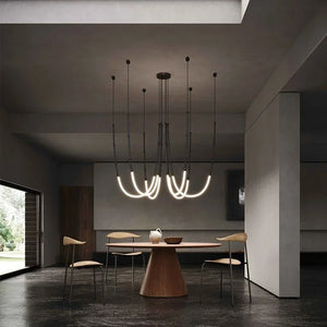 Siliq Sculptural Light with handcrafted silicone forms and metallic segmented cables, single minimalist pendant with glowing silicone tube, dramatic chandelier version of Siliq Light for high ceilings, floor-to-ceiling sculptural lighting installation in modern interior, flexible silicone light tubes emitting soft ambient glow, artistic designer light fixture styled in dining room, contemporary sculptural lighting as statement piece in commercial space.