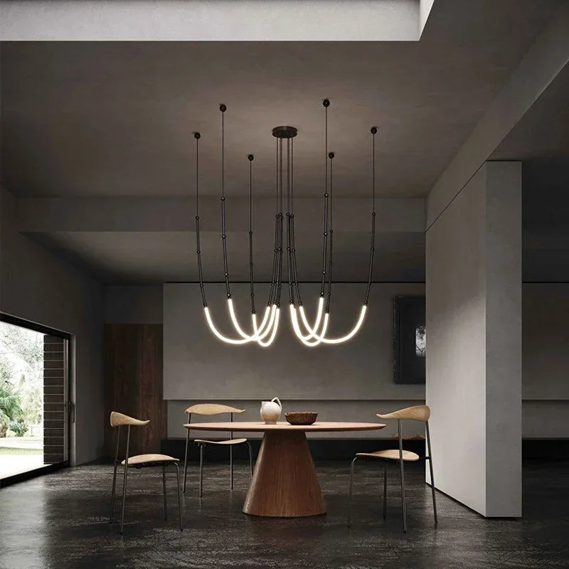 Siliq Sculptural Light with handcrafted silicone forms and metallic segmented cables, single minimalist pendant with glowing silicone tube, dramatic chandelier version of Siliq Light for high ceilings, floor-to-ceiling sculptural lighting installation in modern interior, flexible silicone light tubes emitting soft ambient glow, artistic designer light fixture styled in dining room, contemporary sculptural lighting as statement piece in commercial space.