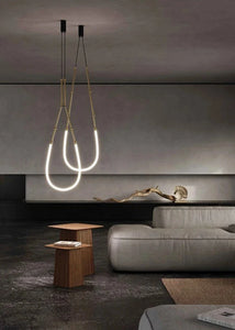 Siliq Sculptural Light with handcrafted silicone forms and metallic segmented cables, single minimalist pendant with glowing silicone tube, dramatic chandelier version of Siliq Light for high ceilings, floor-to-ceiling sculptural lighting installation in modern interior, flexible silicone light tubes emitting soft ambient glow, artistic designer light fixture styled in dining room, contemporary sculptural lighting as statement piece in commercial space.