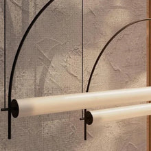 Load image into Gallery viewer, Solari Arc Light with brass arc and linear LED tube, sculptural pendant available in gold or black finish, pair of Solari Arc Lights hanging in modern dining space, minimalist arc pendant styled in office interior, contemporary pendant lighting with sleek LED tube, statement arc light fixture for high ceiling interiors. Modern wall-mounted light fixture with curved design against a textured wall.
