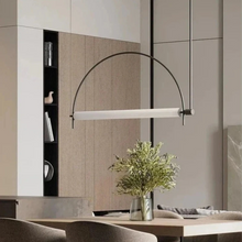 Load image into Gallery viewer, Solari Arc Light with brass arc and linear LED tube, sculptural pendant available in gold or black finish, pair of Solari Arc Lights hanging in modern dining space, minimalist arc pendant styled in office interior, contemporary pendant lighting with sleek LED tube, statement arc light fixture for high ceiling interiors. Modern pendant light hanging above a dining table with a vase of flowers.
