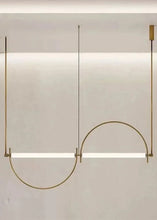 Load image into Gallery viewer, Solari Arc Light with brass arc and linear LED tube, sculptural pendant available in gold or black finish, pair of Solari Arc Lights hanging in modern dining space, minimalist arc pendant styled in office interior, contemporary pendant lighting with sleek LED tube, statement arc light fixture for high ceiling interiors. Modern pendant light fixture with curved design on a neutral background
