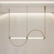 Load image into Gallery viewer, Solari Arc Light with brass arc and linear LED tube, sculptural pendant available in gold or black finish, pair of Solari Arc Lights hanging in modern dining space, minimalist arc pendant styled in office interior, contemporary pendant lighting with sleek LED tube, statement arc light fixture for high ceiling interiors. Modern pendant light fixture with a curved design on a neutral background
