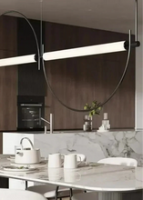 Load image into Gallery viewer, Solari Arc Light with brass arc and linear LED tube, sculptural pendant available in gold or black finish, pair of Solari Arc Lights hanging in modern dining space, minimalist arc pendant styled in office interior, contemporary pendant lighting with sleek LED tube, statement arc light fixture for high ceiling interiors. Modern kitchen with a pendant light fixture above a dining table.
