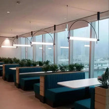 Load image into Gallery viewer, Solari Arc Light with brass arc and linear LED tube, sculptural pendant available in gold or black finish, pair of Solari Arc Lights hanging in modern dining space, minimalist arc pendant styled in office interior, contemporary pendant lighting with sleek LED tube, statement arc light fixture for high ceiling interiors. Restaurant Interior
