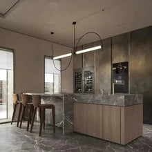 Load image into Gallery viewer, Solari Arc Light with brass arc and linear LED tube, sculptural pendant available in gold or black finish, pair of Solari Arc Lights hanging in modern dining space, minimalist arc pendant styled in office interior, contemporary pendant lighting with sleek LED tube, statement arc light fixture for high ceiling interiors. Modern kitchen with marble island and bar stools
