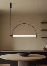 Load image into Gallery viewer, Solari Arc Light with brass arc and linear LED tube, sculptural pendant available in gold or black finish, pair of Solari Arc Lights hanging in modern dining space, minimalist arc pendant styled in office interior, contemporary pendant lighting with sleek LED tube, statement arc light fixture for high ceiling interiors. Modern pendant light hanging above a dining table with a neutral background
