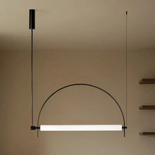 Load image into Gallery viewer, Solari Arc Light with brass arc and linear LED tube, sculptural pendant available in gold or black finish, pair of Solari Arc Lights hanging in modern dining space, minimalist arc pendant styled in office interior, contemporary pendant lighting with sleek LED tube, statement arc light fixture for high ceiling interiors. Modern pendant light with a curved design hanging against a neutral wall.
