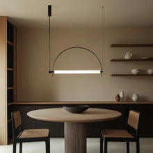 Load image into Gallery viewer, Solari Arc Light with brass arc and linear LED tube, sculptural pendant available in gold or black finish, pair of Solari Arc Lights hanging in modern dining space, minimalist arc pendant styled in office interior, contemporary pendant lighting with sleek LED tube, statement arc light fixture for high ceiling interiors. Modern dining area with a round table, chairs, and minimalist lighting fixture.
