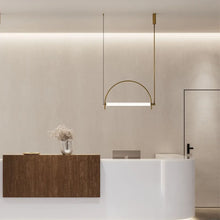 Load image into Gallery viewer, Solari Arc Light with brass arc and linear LED tube, sculptural pendant available in gold or black finish, pair of Solari Arc Lights hanging in modern dining space, minimalist arc pendant styled in office interior, contemporary pendant lighting with sleek LED tube, statement arc light fixture for high ceiling interiors. Modern interior design with a reception desk and hanging light fixture.
